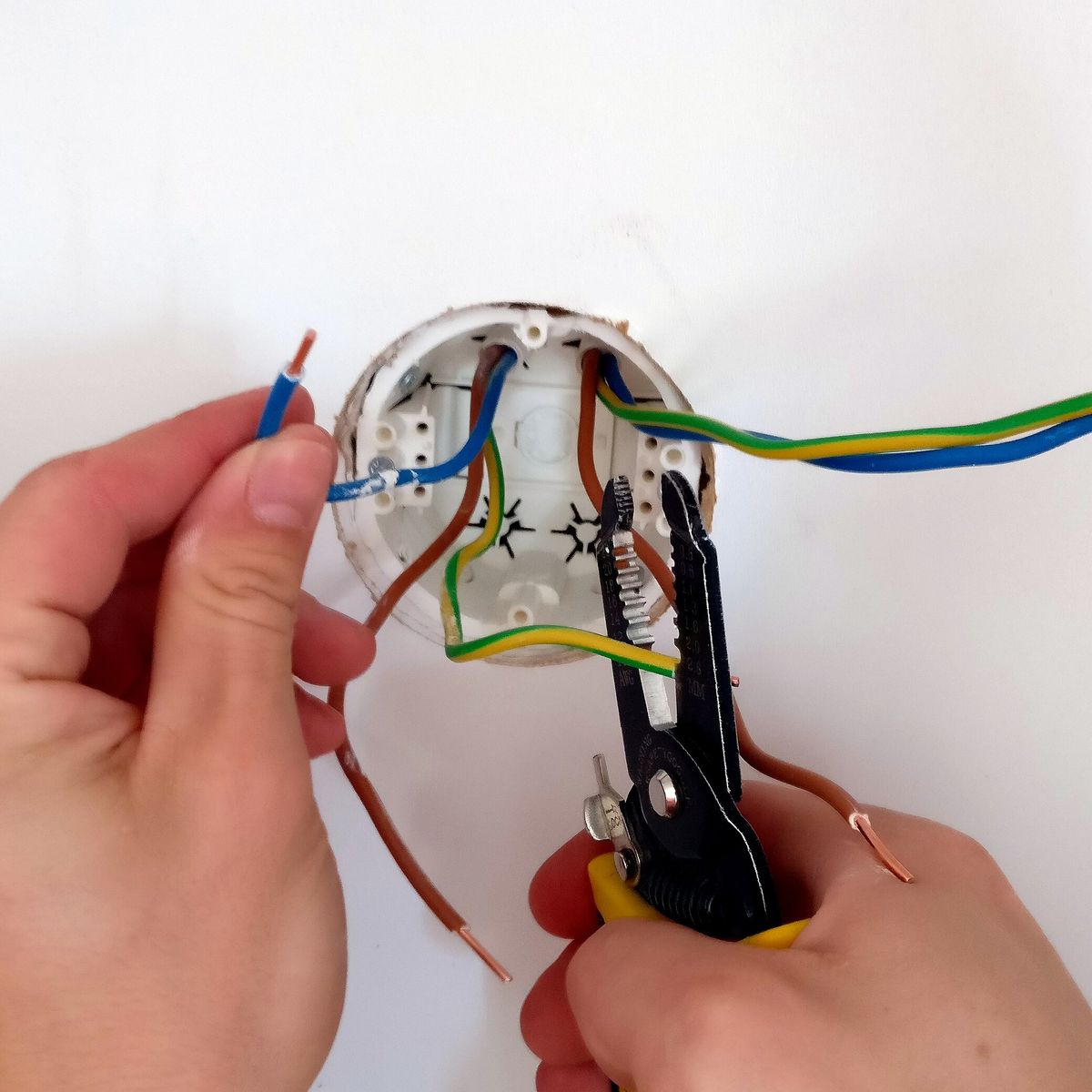 Een elektricien stript de draden in een inbouwdoos
