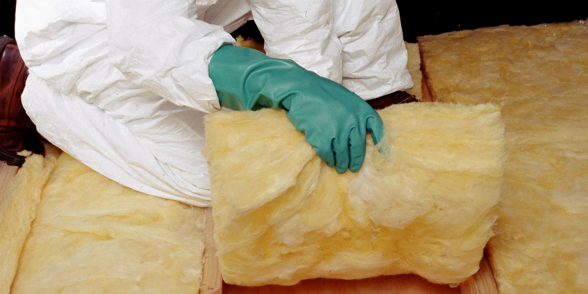 Een vakman legt glaswol tussen de balken van een zoldervloer