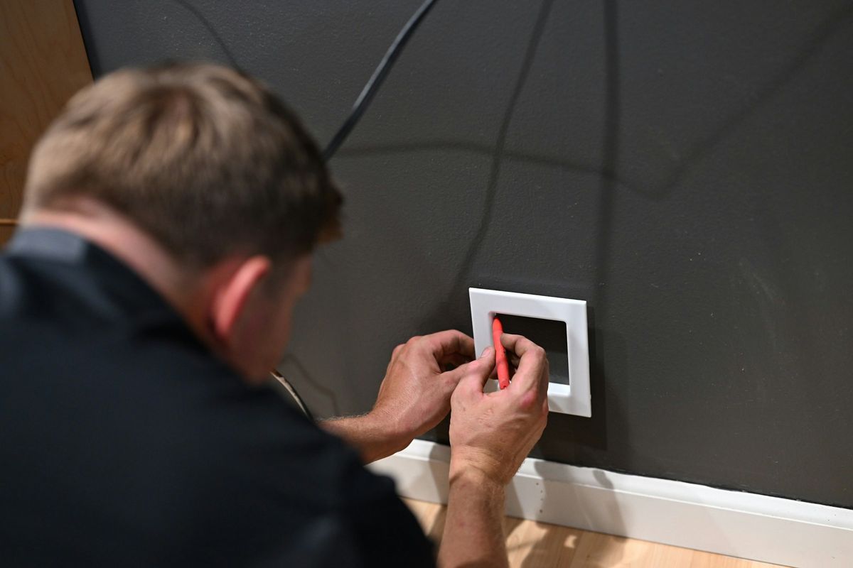 Een elektricien monteert een schakelaar op een donkere muur